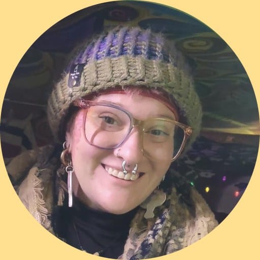 Sarah Abear, smiling, in a knitted hat and patterned scarf